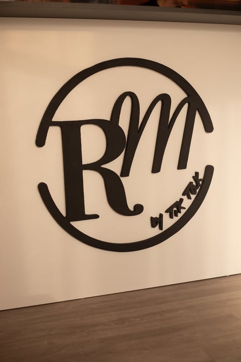 Black line drawing logo with letters R, M inside a circular oval shape on a cream-colored wall