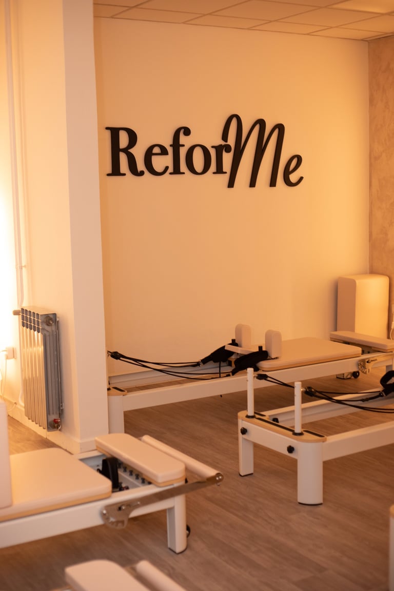 ReforMe studio interior with white Pilates reformer beds and black wall text signage