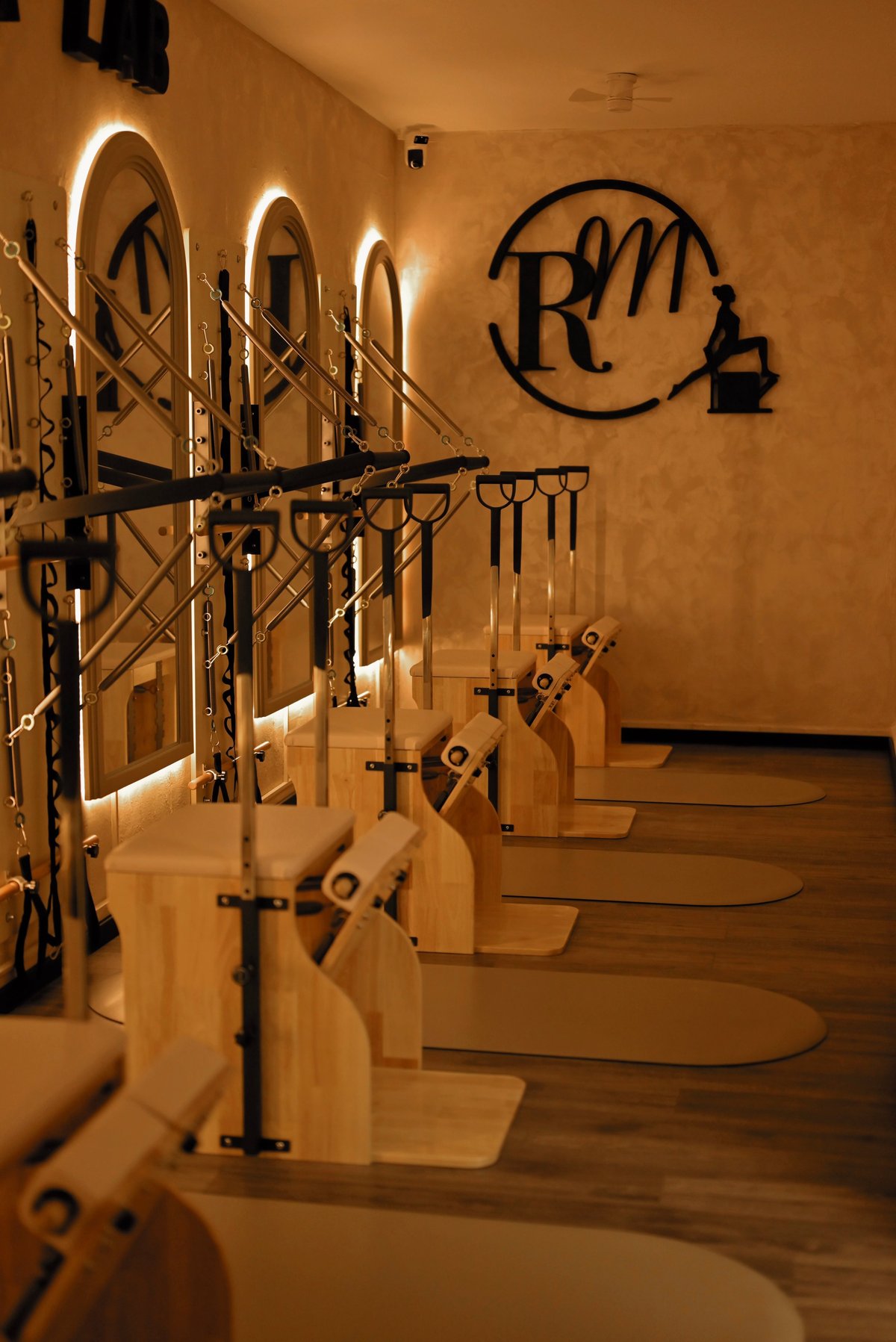 Row of wooden Pilates reformer machines with metal frames lined up in an indoor studio with warm lighting