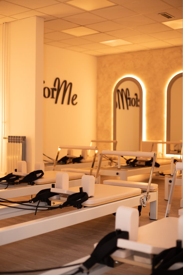 Modern pilates studio with ofMe signage, Pilates reformers with black straps, arched neon mirrors, and warm ambient lighting