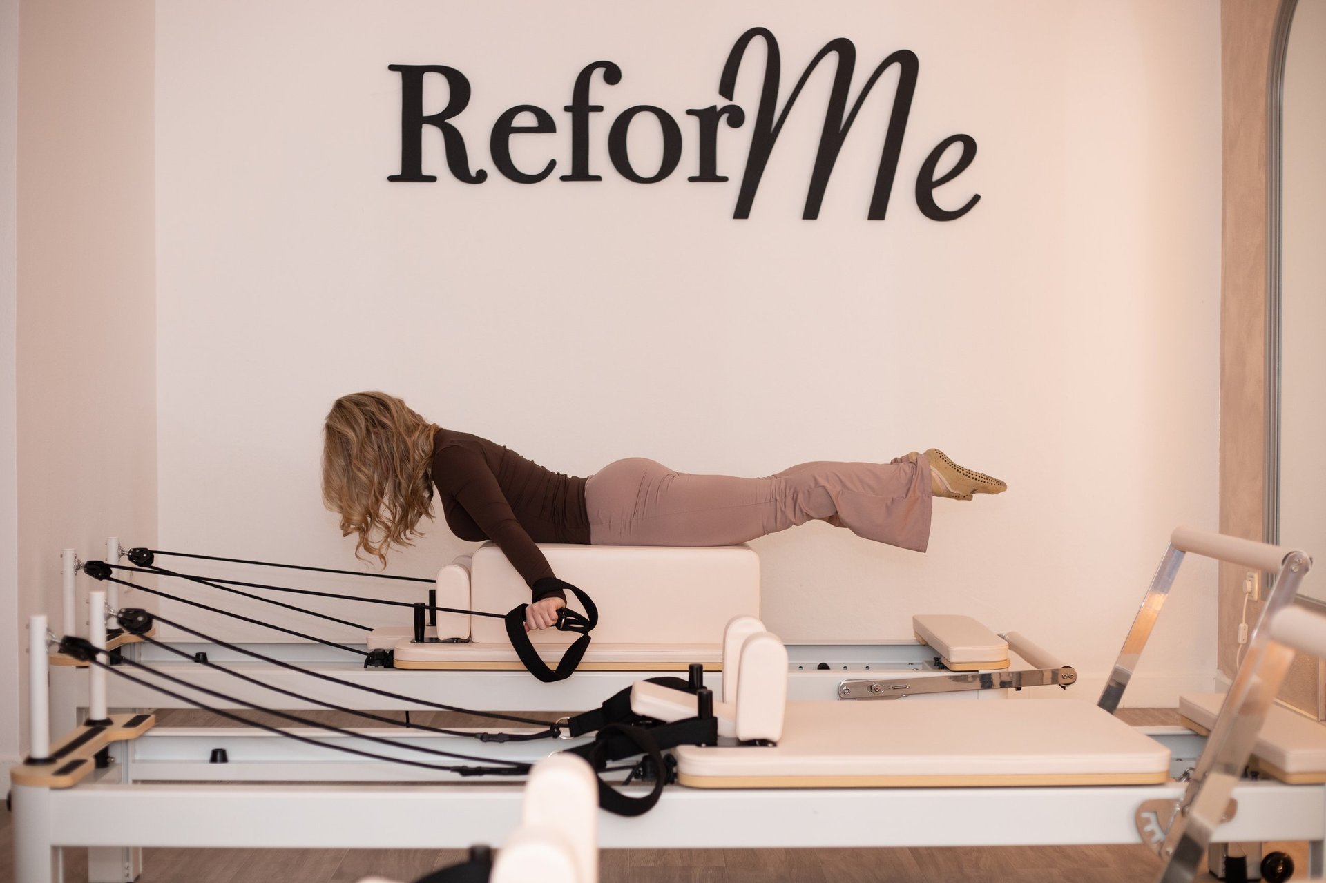 Woman performing a plank exercise on a Reformers pilates machine with springs visible beneath her body