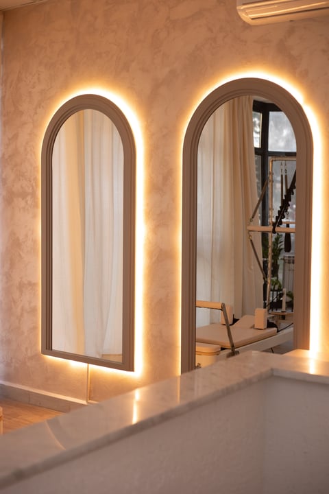 Two arched mirrors with LED backlighting mounted on a textured beige wall in a modern interior space