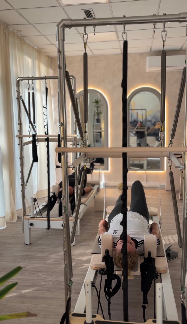 Woman performing pilates reformer exercise in a bright studio with mirrored walls and hanging resistance bands